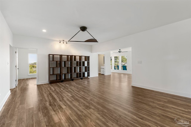 unfurnished living room featuring dark wood-type flooring and ceiling fan