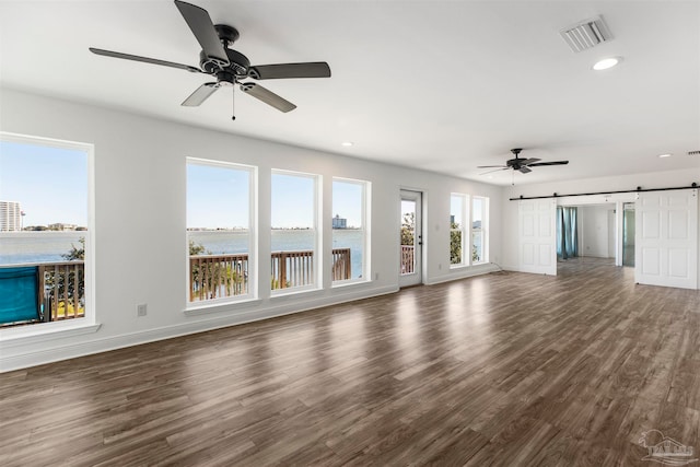 unfurnished living room with dark hardwood / wood-style floors, a barn door, a water view, and ceiling fan