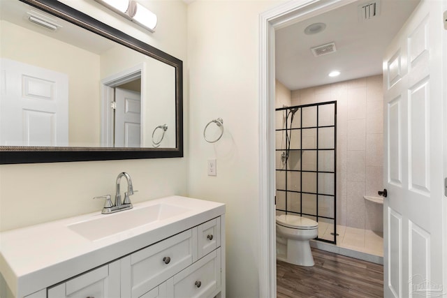 bathroom with a tile shower, toilet, wood-type flooring, and vanity