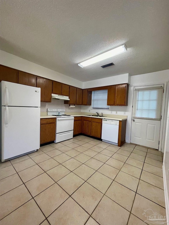 kitchen with a textured ceiling, light tile patterned flooring, white appliances, and sink