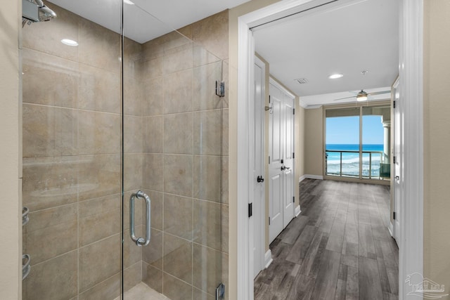 bathroom with a water view, a shower with door, ceiling fan, and hardwood / wood-style floors