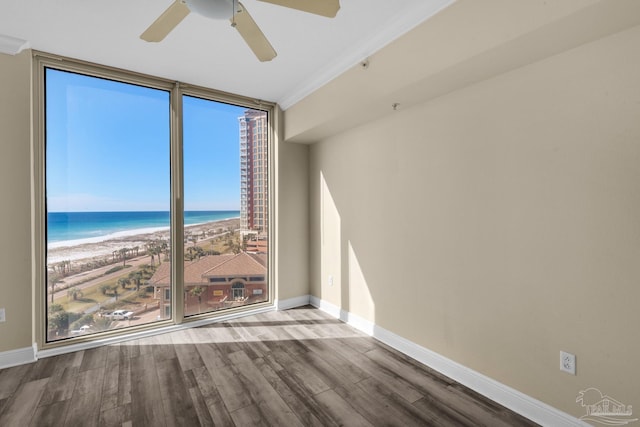 empty room with a beach view, a water view, ceiling fan, ornamental molding, and floor to ceiling windows