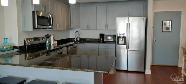 kitchen featuring kitchen peninsula, stainless steel appliances, a kitchen bar, dark stone counters, and sink