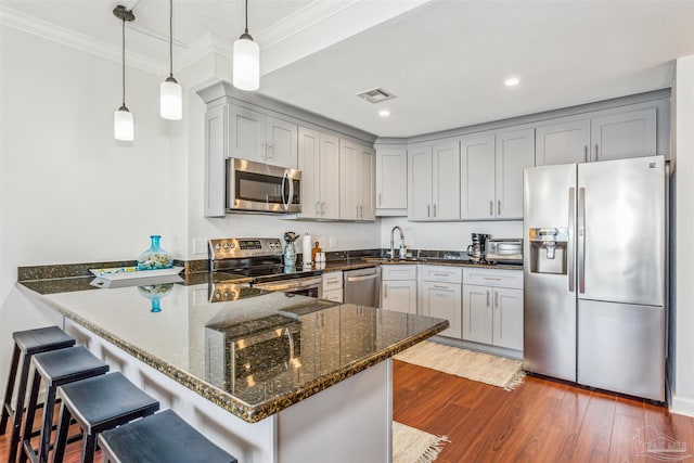 kitchen featuring kitchen peninsula, stainless steel appliances, decorative light fixtures, dark stone countertops, and crown molding