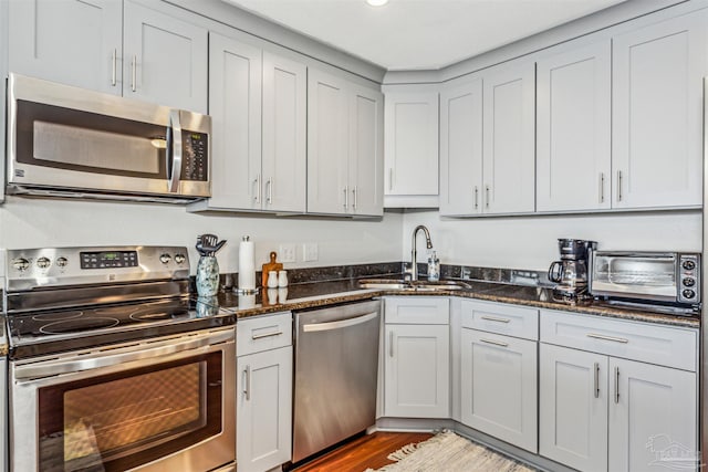 kitchen with sink, hardwood / wood-style floors, appliances with stainless steel finishes, and dark stone countertops