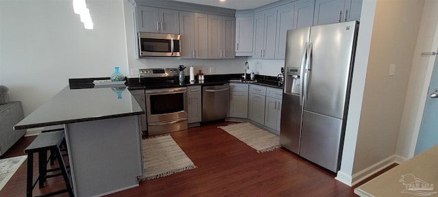 kitchen featuring a breakfast bar, kitchen peninsula, sink, appliances with stainless steel finishes, and dark hardwood / wood-style flooring