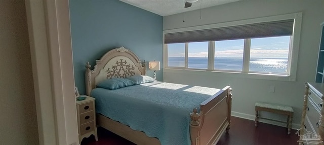 bedroom featuring ceiling fan, dark wood-type flooring, a textured ceiling, and a water view