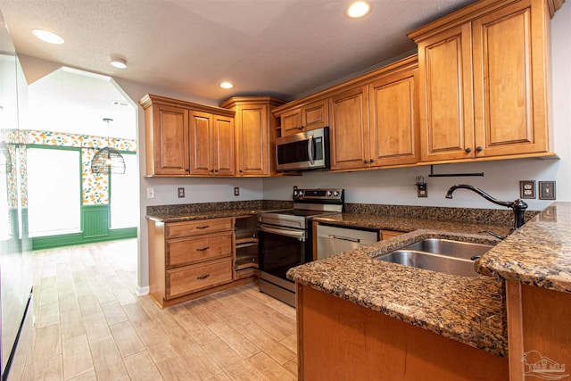 kitchen featuring dark stone countertops, sink, light wood-type flooring, and stainless steel appliances