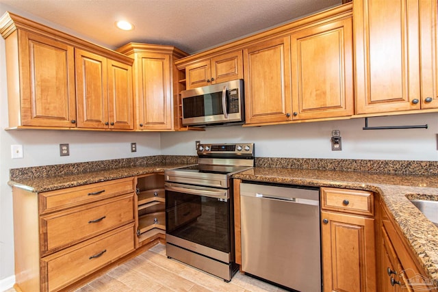 kitchen featuring light wood-type flooring, stainless steel appliances, and dark stone countertops