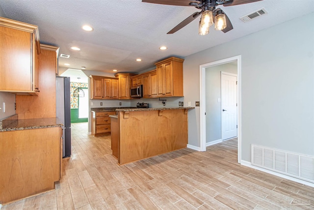 kitchen featuring kitchen peninsula, a kitchen breakfast bar, light wood-type flooring, and stainless steel appliances