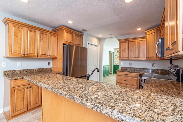 kitchen with dark stone counters, light wood-type flooring, a textured ceiling, kitchen peninsula, and stainless steel appliances