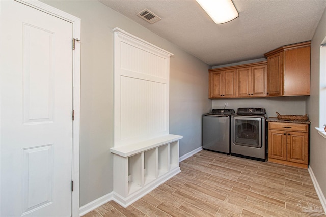 clothes washing area with cabinets, a textured ceiling, light hardwood / wood-style floors, and washer and clothes dryer