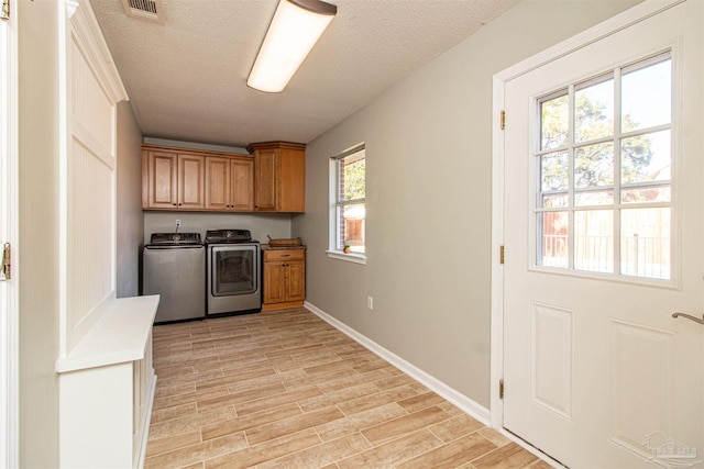 laundry area featuring washer and dryer, light hardwood / wood-style flooring, cabinets, and a textured ceiling