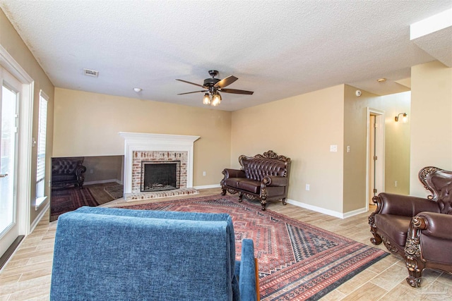 living room featuring ceiling fan, light hardwood / wood-style floors, a textured ceiling, and a brick fireplace