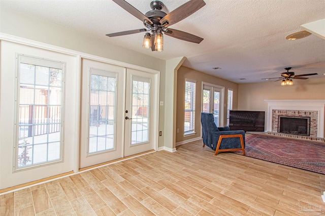 interior space featuring french doors, a textured ceiling, ceiling fan, a fireplace, and light hardwood / wood-style floors