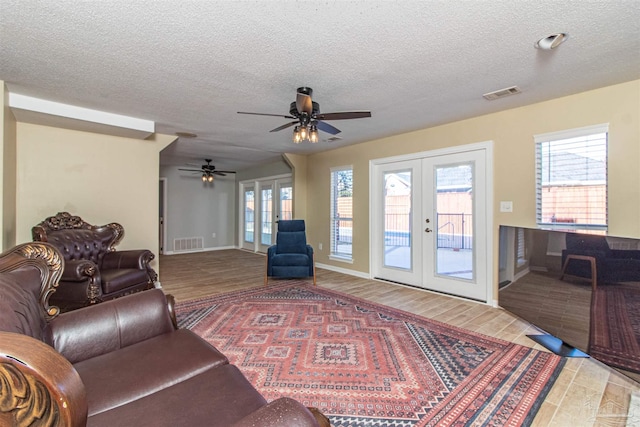 living room with french doors, a textured ceiling, ceiling fan, and wood-type flooring