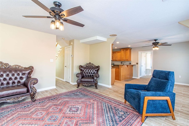 living room with ceiling fan, a textured ceiling, and light wood-type flooring