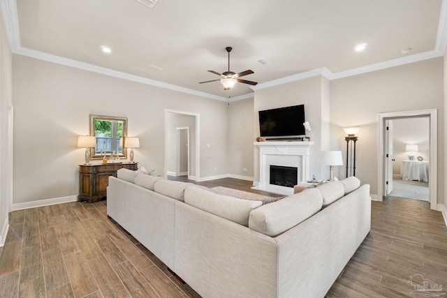 living room with a ceiling fan, a fireplace, wood finished floors, baseboards, and ornamental molding