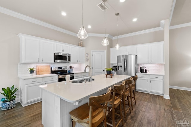 kitchen featuring crown molding, appliances with stainless steel finishes, a sink, decorative backsplash, and a center island with sink