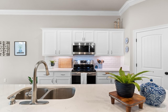 kitchen featuring tasteful backsplash, a sink, ornamental molding, stainless steel appliances, and white cabinetry