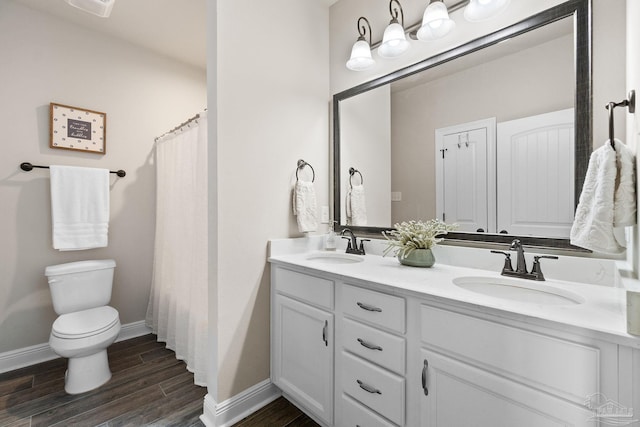 bathroom featuring double vanity, a sink, wood finished floors, and toilet