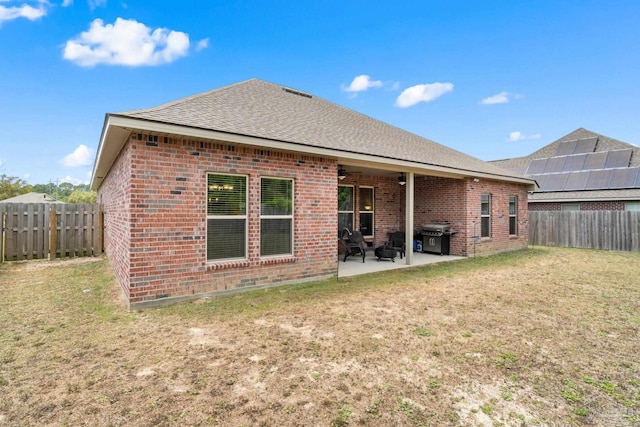 back of property with a patio, a fenced backyard, brick siding, a shingled roof, and a yard