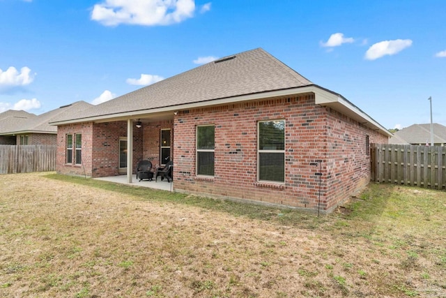 rear view of property featuring a fenced backyard, roof with shingles, brick siding, a patio area, and a lawn