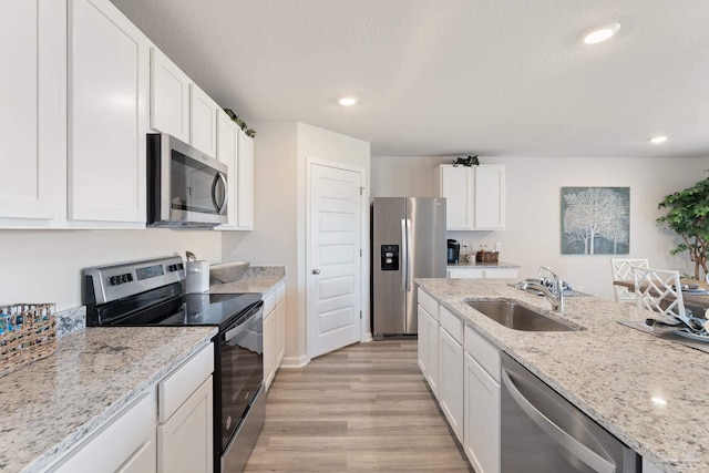 kitchen with white cabinets, light stone counters, appliances with stainless steel finishes, light wood-type flooring, and sink