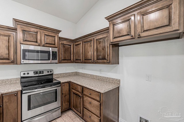 kitchen with appliances with stainless steel finishes, lofted ceiling, and dark brown cabinetry