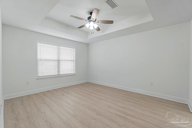 unfurnished room featuring a raised ceiling, ceiling fan, and light hardwood / wood-style floors