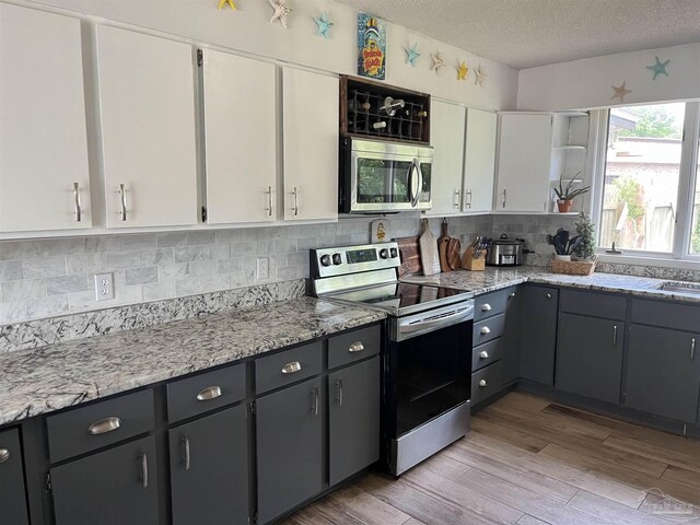 kitchen featuring appliances with stainless steel finishes, tasteful backsplash, light hardwood / wood-style floors, a textured ceiling, and white cabinetry