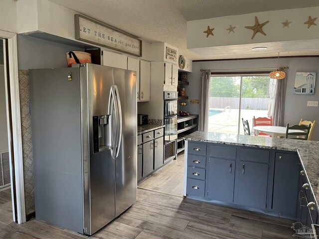 kitchen featuring stainless steel appliances, white cabinets, pendant lighting, hardwood / wood-style floors, and a textured ceiling