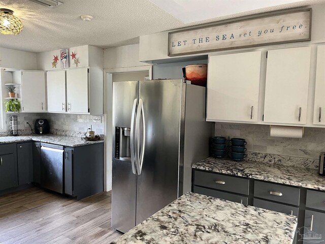 kitchen featuring white cabinetry, tasteful backsplash, stainless steel appliances, light stone countertops, and light hardwood / wood-style flooring