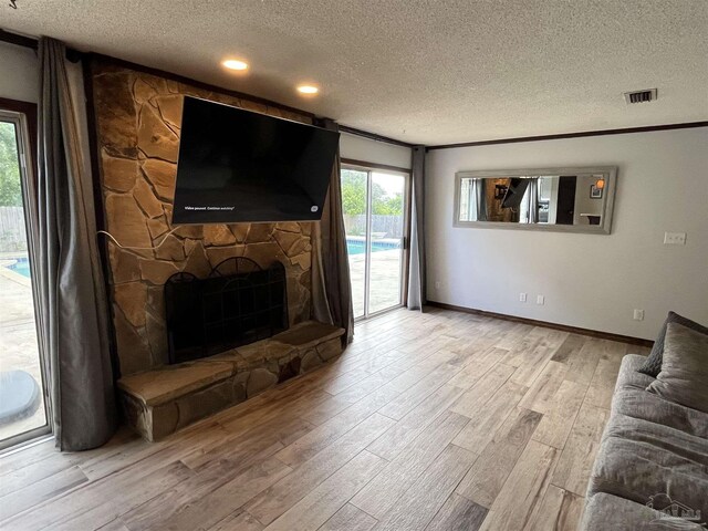 living room featuring light hardwood / wood-style floors, ornamental molding, a fireplace, and a textured ceiling