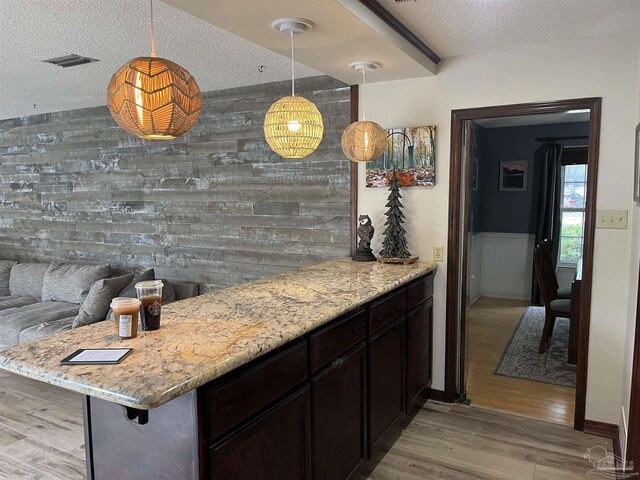 kitchen with pendant lighting, wood walls, light wood-type flooring, and a textured ceiling