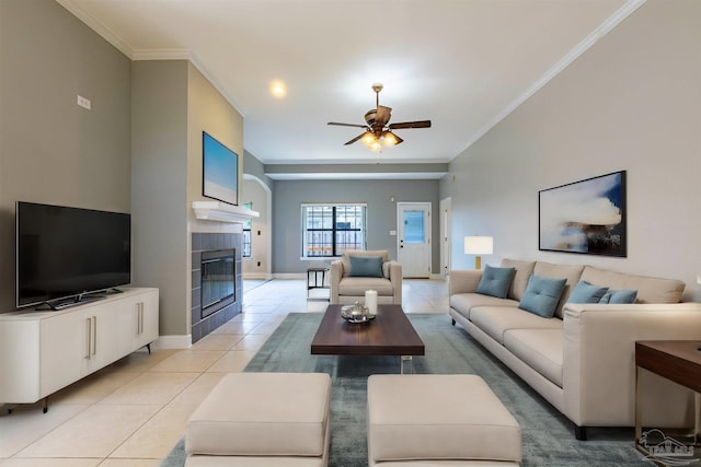 living room featuring crown molding, ceiling fan, a tiled fireplace, and light tile patterned floors