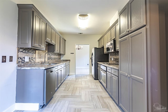 kitchen with appliances with stainless steel finishes, sink, gray cabinetry, backsplash, and light stone countertops