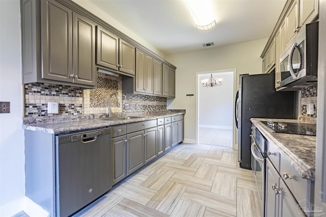 kitchen featuring appliances with stainless steel finishes, sink, dark stone countertops, backsplash, and a notable chandelier