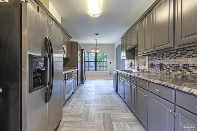 kitchen featuring pendant lighting, sink, dark stone countertops, stainless steel appliances, and a chandelier