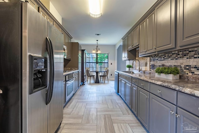 kitchen with gray cabinets, appliances with stainless steel finishes, pendant lighting, sink, and dark stone countertops