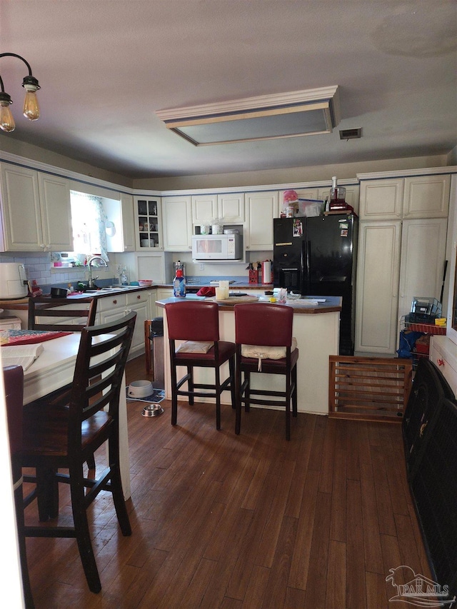 8176 Camelford Dr, Pensacola, FL 32506 - kitchen featuring white microwave, visible vents, dark wood finished floors, backsplash, and black fridge
