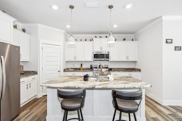 kitchen featuring appliances with stainless steel finishes, an island with sink, pendant lighting, hardwood / wood-style floors, and sink