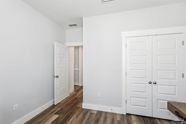 unfurnished bedroom featuring baseboards, visible vents, dark wood finished floors, and a closet