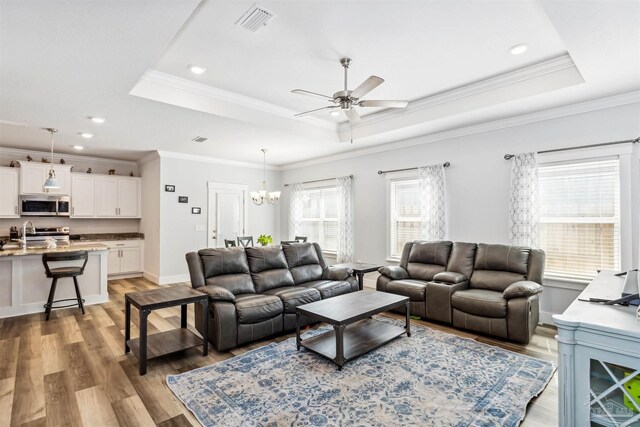 living room with ornamental molding, ceiling fan with notable chandelier, a tray ceiling, and hardwood / wood-style flooring