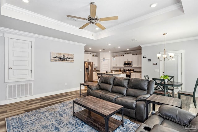 living room with ceiling fan with notable chandelier, a tray ceiling, hardwood / wood-style flooring, and crown molding