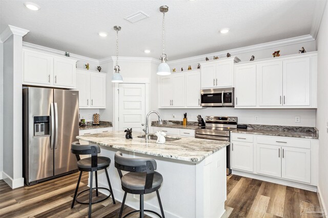 kitchen with pendant lighting, a center island with sink, stainless steel appliances, and white cabinetry