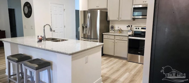 kitchen with sink, stainless steel appliances, light stone counters, light hardwood / wood-style floors, and a kitchen island with sink