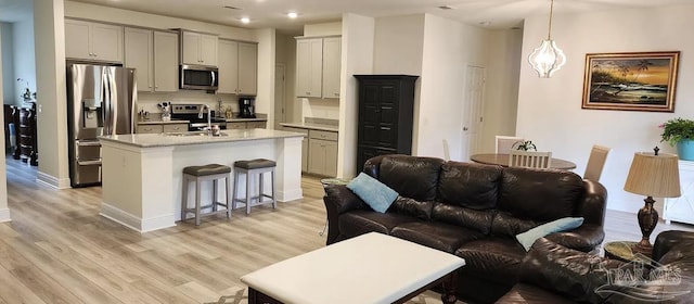 kitchen with hanging light fixtures, stainless steel appliances, a kitchen island with sink, a breakfast bar, and light wood-type flooring