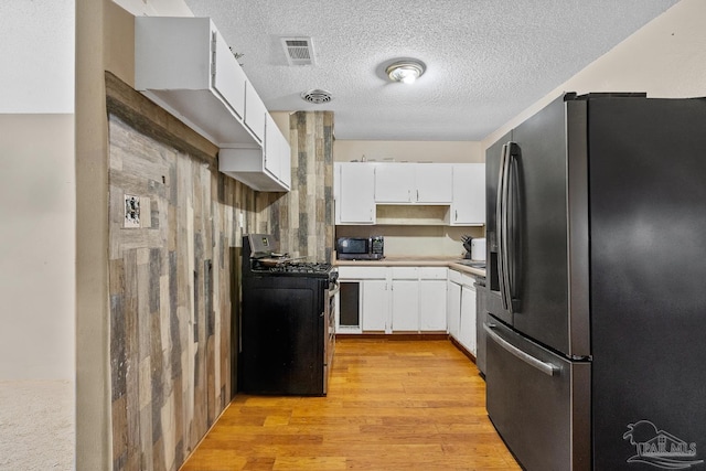 kitchen featuring gas stove, stainless steel fridge, white cabinetry, and light wood-type flooring