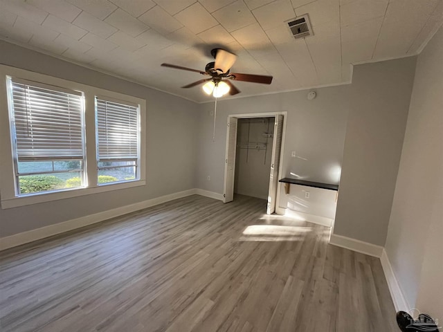 unfurnished bedroom with visible vents, wood finished floors, a closet, crown molding, and baseboards